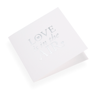 Eine Faltkarte aus 100% Baumwollpapier und der Grösse 14.5 x 14.5 cm von Bookbinders Design, mit dem Spruch «Love is...» aufgedruckt.