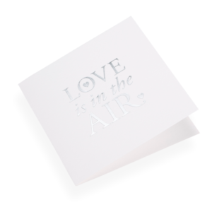Eine Faltkarte aus 100% Baumwollpapier und der Grösse 14.5 x 14.5 cm von Bookbinders Design, mit dem Spruch «Love is...» aufgedruckt.