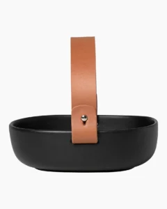 Die kleine Servierplatte Pikku Koppa besteht aus braunem Steingut mit einer mattschwarzen Glasur und ist spülmaschinen-, ofen-, mikrowellen- und gefrierschrankfest. Der Ledergriff lässt sich leicht abnehmen und sollte vor dem Waschen der Platte abgenommen werden.